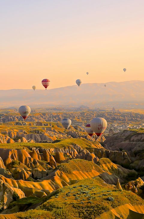Hot air balloons float over mountainous landscapes
