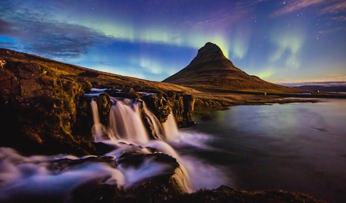 Northern Lights in the sky above a waterfall and mountainous landscape