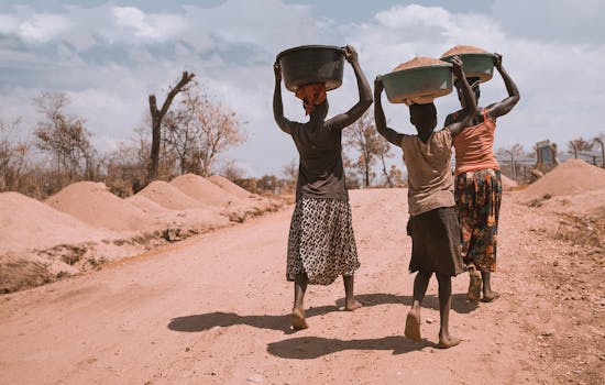 Three people carry supplies along a dirt track in Africa